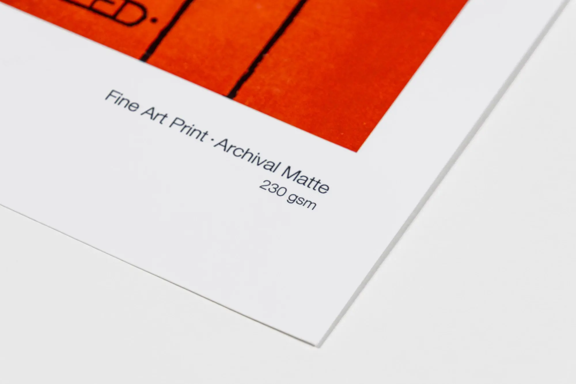 Close-up corner of archival matte fine art print with vibrant orange and black graphic art.